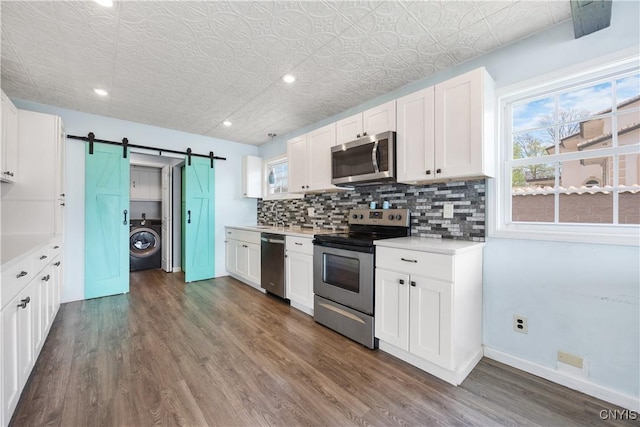 1019 State Route 49, Constantia, NY 13028 - kitchen with appliances with stainless steel finishes, washer / clothes dryer, backsplash, a barn door, and dark wood-style flooring