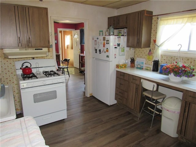 kitchen with white appliances, under cabinet range hood, dark wood finished floors, light countertops, and wallpapered walls