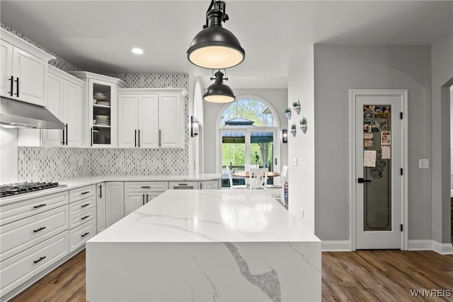 3750 Transit Rd, Orchard Park, NY 14127 - kitchen with under cabinet range hood, a kitchen island, white cabinets, black stovetop, and backsplash