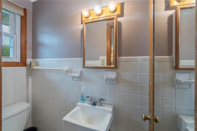 bathroom with a sink, toilet, tile walls, and a wainscoted wall