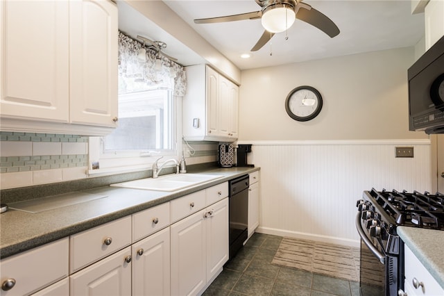 kitchen with black appliances, a sink, wainscoting, a ceiling fan, and white cabinetry