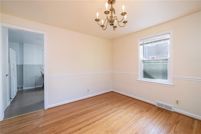 spare room featuring a chandelier, light wood finished floors, and baseboards