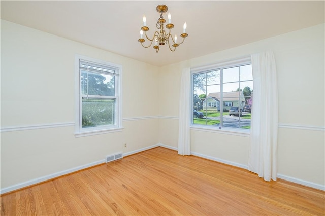 spare room with a chandelier, light wood-style floors, baseboards, and healthy amount of natural light