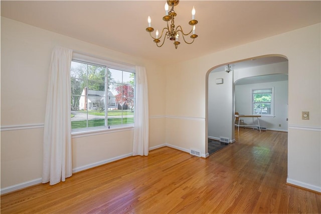 unfurnished dining area with arched walkways, a chandelier, wood finished floors, and baseboards
