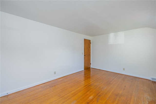 empty room with light wood finished floors, baseboards, and vaulted ceiling