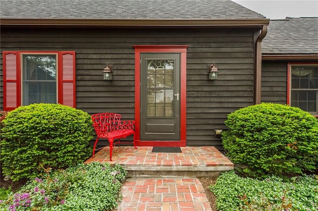 view of exterior entry featuring roof with shingles