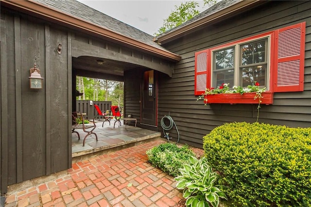 view of exterior entry with a shingled roof and a patio area