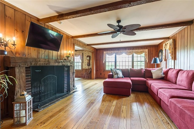 living room with wood walls, beamed ceiling, light wood finished floors, ceiling fan, and a brick fireplace