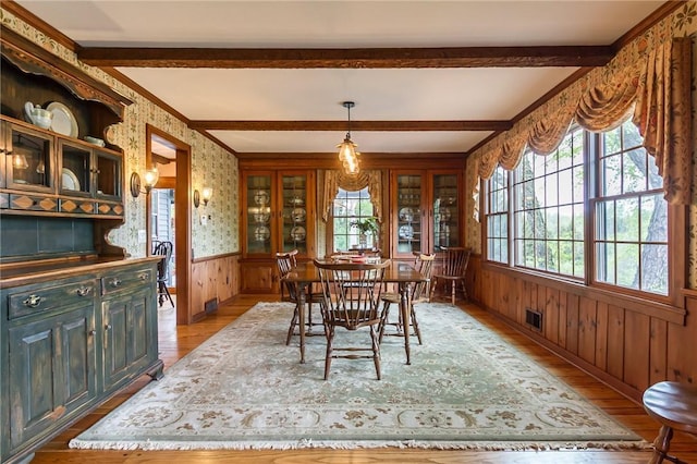 dining room with light wood-style floors, wainscoting, beamed ceiling, wallpapered walls, and wooden walls