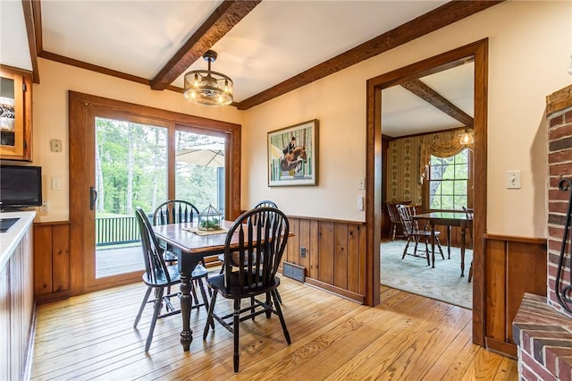 dining area with light wood-style floors, beam ceiling, wainscoting, a chandelier, and wooden walls
