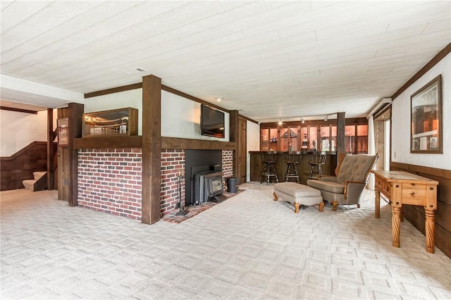living room featuring carpet floors, wooden walls, stairs, a wood stove, and a bar