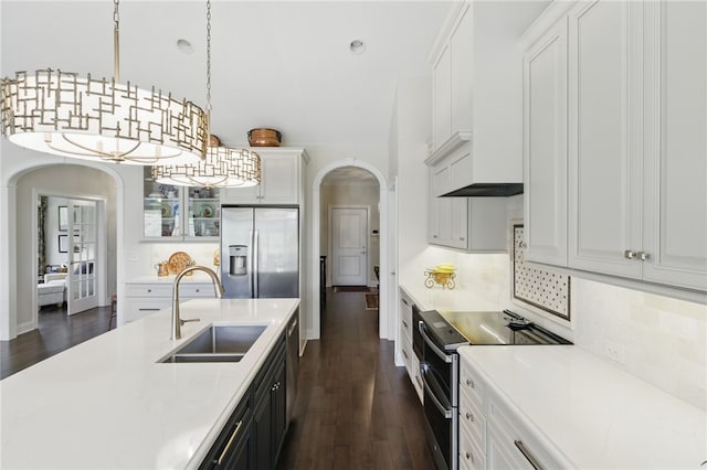 kitchen featuring appliances with stainless steel finishes, arched walkways, a sink, dark wood-type flooring, and pendant lighting