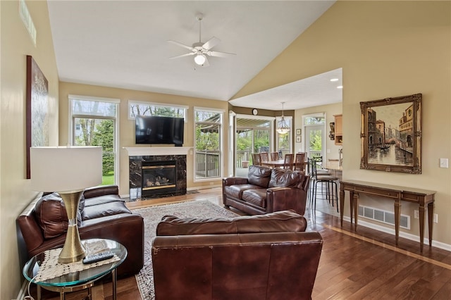 living area featuring wood finished floors, a ceiling fan, vaulted ceiling, a high end fireplace, and baseboards