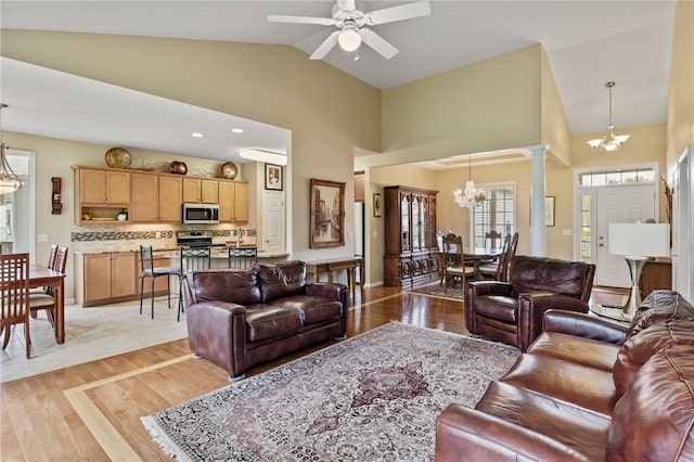 living area with a chandelier, ceiling fan, decorative columns, light wood finished floors, and high vaulted ceiling