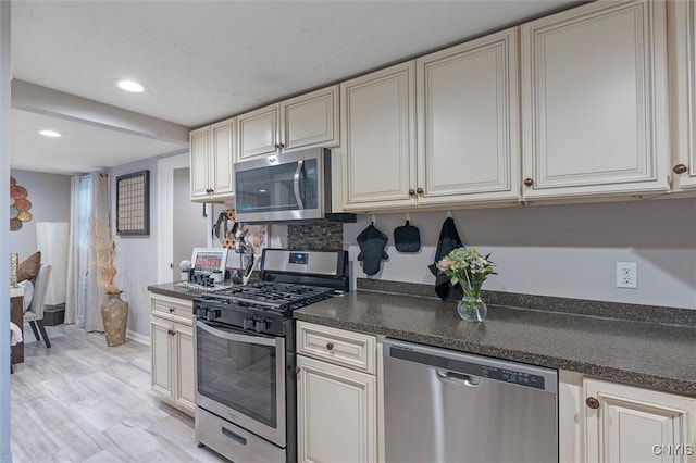 kitchen featuring stainless steel appliances, dark countertops, recessed lighting, baseboards, and cream cabinets