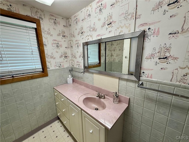 bathroom with tile walls, wainscoting, vanity, and wallpapered walls