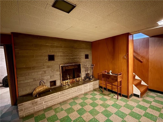 living area featuring a stone fireplace, stairs, tile patterned floors, and wooden walls