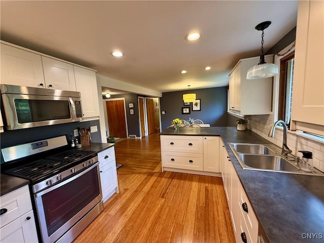 kitchen featuring stainless steel appliances, a sink, dark countertops, light wood-style floors, and recessed lighting