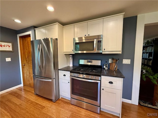 kitchen featuring stainless steel appliances, baseboards, dark countertops, light wood-style floors, and white cabinetry