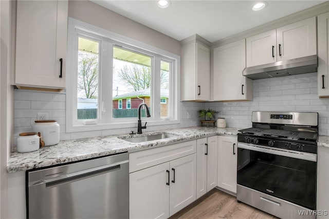 kitchen with stainless steel appliances, a sink, under cabinet range hood, light wood-style floors, and light stone counters