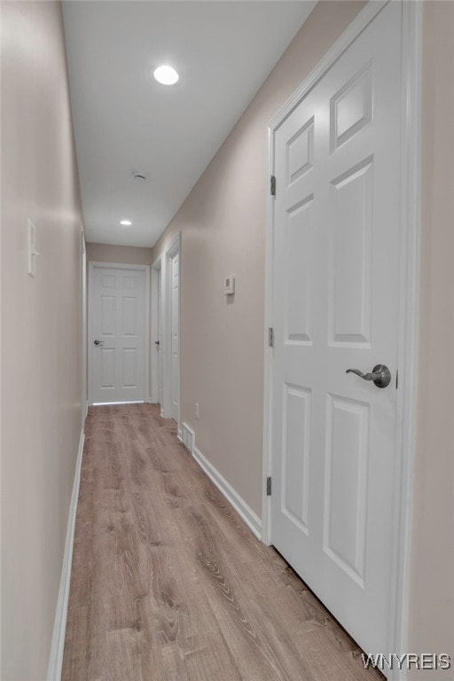hall featuring baseboards, light wood-type flooring, and recessed lighting