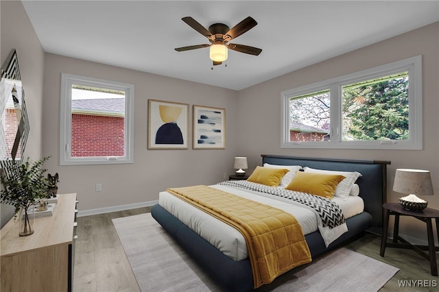 bedroom with multiple windows, wood finished floors, baseboards, and a ceiling fan