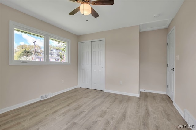 unfurnished bedroom with light wood-type flooring, attic access, a closet, baseboards, and a ceiling fan