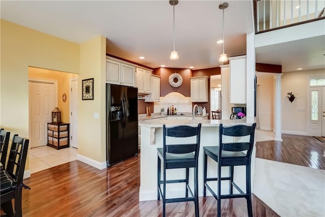 kitchen with black refrigerator with ice dispenser, light wood-style flooring, ornate columns, a peninsula, and light countertops
