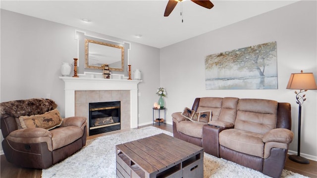 living area with wood finished floors, ceiling fan, a tile fireplace, and baseboards