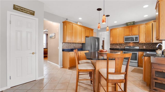kitchen with appliances with stainless steel finishes, a kitchen island, light tile patterned floors, tasteful backsplash, and a kitchen bar