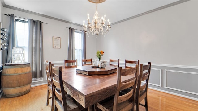 dining room with a chandelier, light wood-style flooring, crown molding, and wainscoting