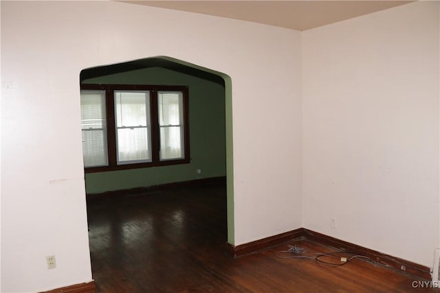 spare room with hardwood / wood-style floors, baseboards, and arched walkways