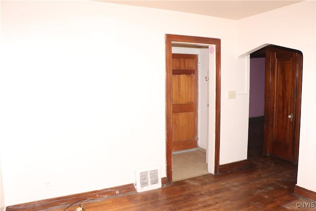 unfurnished room featuring dark wood-style flooring, baseboards, and arched walkways