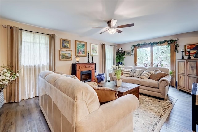 living room featuring a ceiling fan, dark wood-style flooring, and a glass covered fireplace