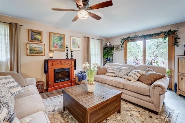 living room featuring a ceiling fan, light wood-type flooring, and a glass covered fireplace