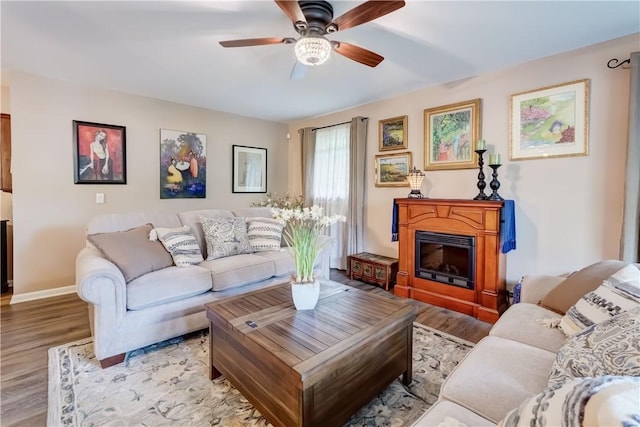 living room featuring wood finished floors, ceiling fan, baseboards, and a glass covered fireplace