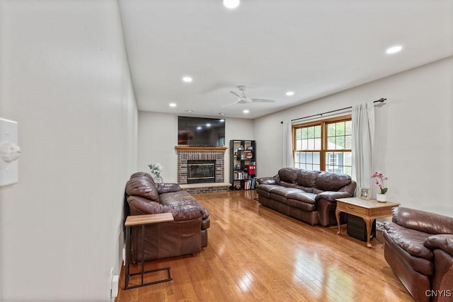 living area with ceiling fan, light wood finished floors, recessed lighting, and a brick fireplace