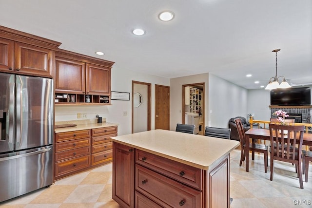 kitchen with stainless steel fridge, light countertops, recessed lighting, hanging light fixtures, and brown cabinets