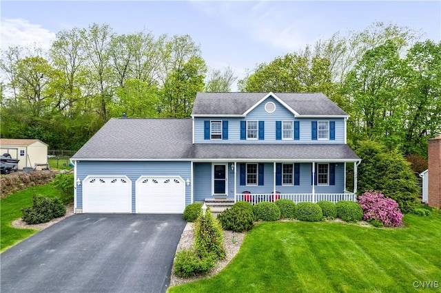 colonial-style house featuring a garage, asphalt driveway, covered porch, a front yard, and roof with shingles