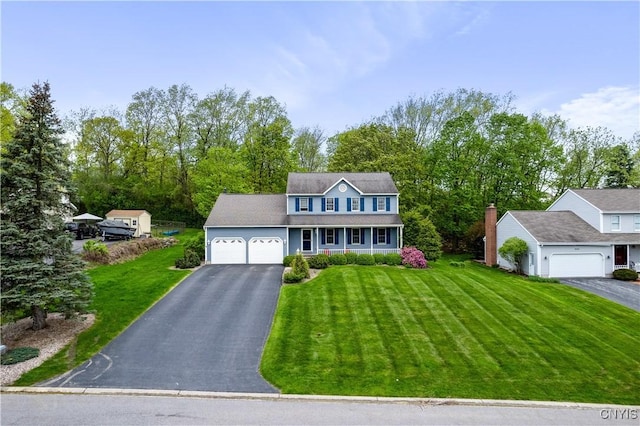 colonial-style house featuring driveway, a garage, a front lawn, and covered porch
