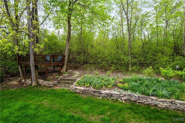 view of green lawn with a wooden deck and a view of trees