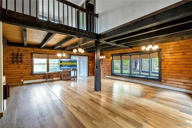 353 Campbell Rd, Sweden, NY 14420 - unfurnished living room featuring a chandelier, wooden walls, wood-type flooring, beamed ceiling, and a baseboard radiator