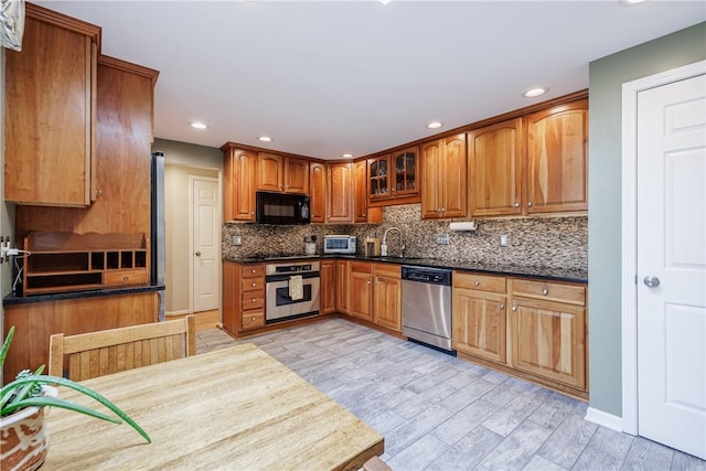kitchen featuring stainless steel appliances, a sink, tasteful backsplash, recessed lighting, and dark countertops