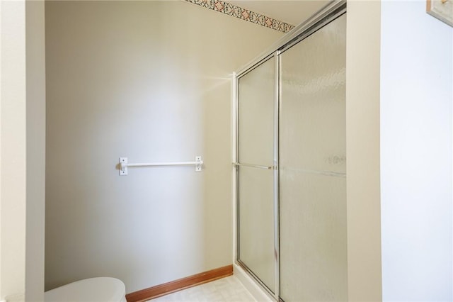 bathroom with toilet, a shower with shower door, and baseboards