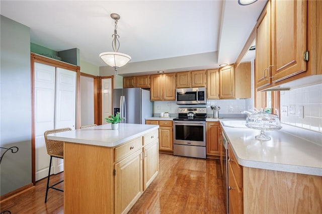 kitchen featuring stainless steel appliances, light countertops, light wood finished floors, tasteful backsplash, and a sink