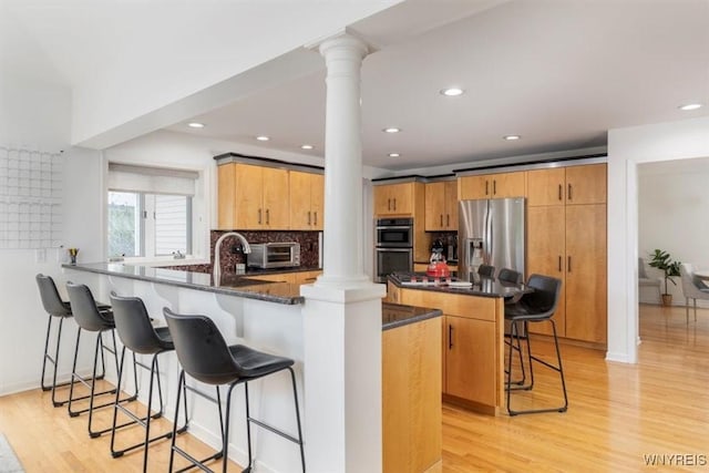 kitchen with decorative columns, a peninsula, appliances with stainless steel finishes, a kitchen breakfast bar, and recessed lighting