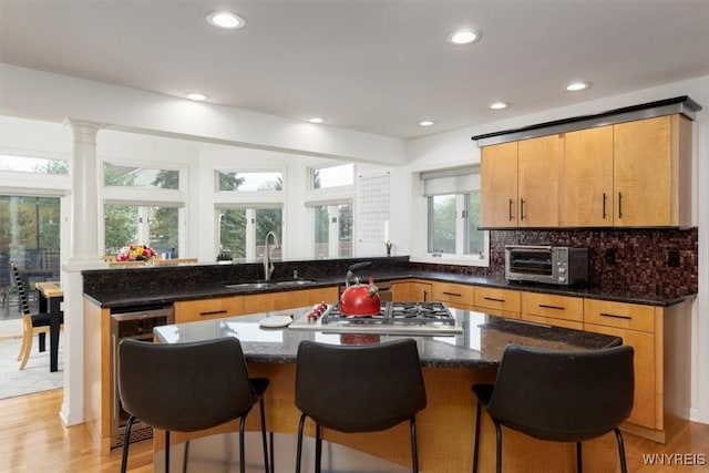 kitchen with a sink, stainless steel gas stovetop, dark stone counters, recessed lighting, and a kitchen island