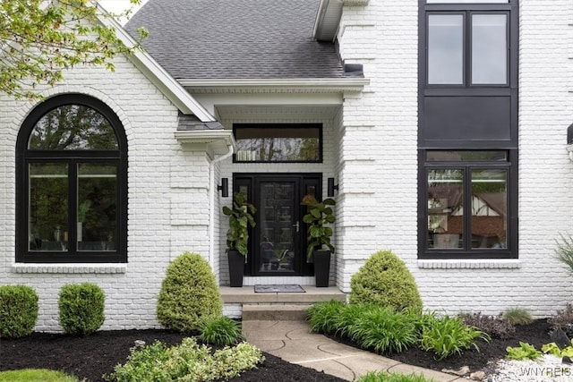 doorway to property with brick siding and roof with shingles