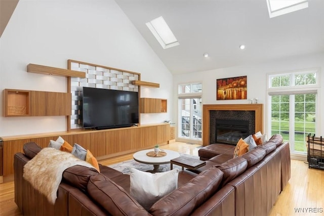 living room with a skylight, high vaulted ceiling, light wood-type flooring, a glass covered fireplace, and recessed lighting