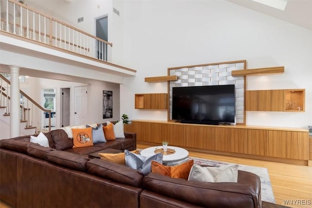 living area with a high ceiling, light wood-style flooring, and stairway